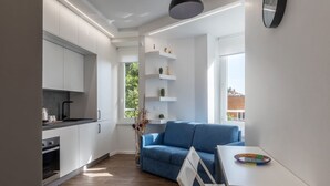 A modern kitchen with white cabinets, a blue sofa, and a dining table with a colorful plate. - GuestHost - Monteverde Classy Apartment (Roma)