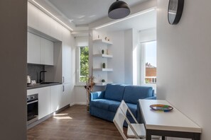 A modern kitchen with white cabinets, a blue sofa, and a dining table with a colorful plate.