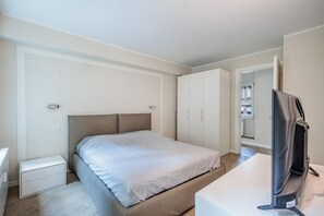 Quarto com uma cama, televisão, guarda-roupa e mesa de cabeceira.