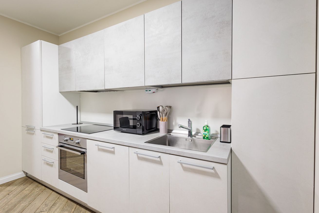 A modern kitchen with white cabinetry, a built-in oven, a microwave, and a stainless steel sink.