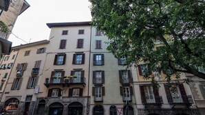 Vista de una calle con edificios de varios pisos, algunos con balcones, y un árbol en primer plano.