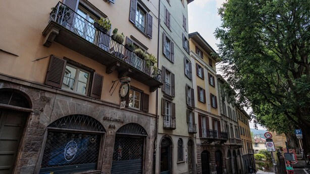 Una hilera de edificios históricos con ventanas de arco y balcones, una calle adoquinada y una señal de no estacionamiento.