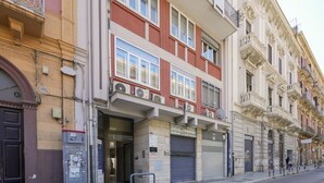 Eine Reihe mehrstöckiger Gebäude mit Balkonen und großen Fenstern, vor ihnen eine Straße.