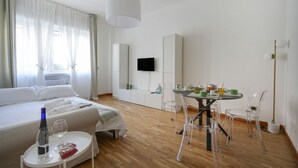 Ein Hotelzimmer mit einem Bett, einem Esstisch mit Stühlen, einem Fernseher und einem Fenster mit Vorhängen.