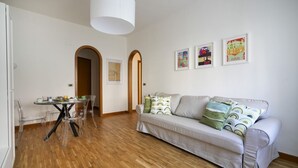 Ein Wohnzimmer mit einer Couch, einem Esstisch mit Stühlen und gerahmten Kunstwerken an der Wand.