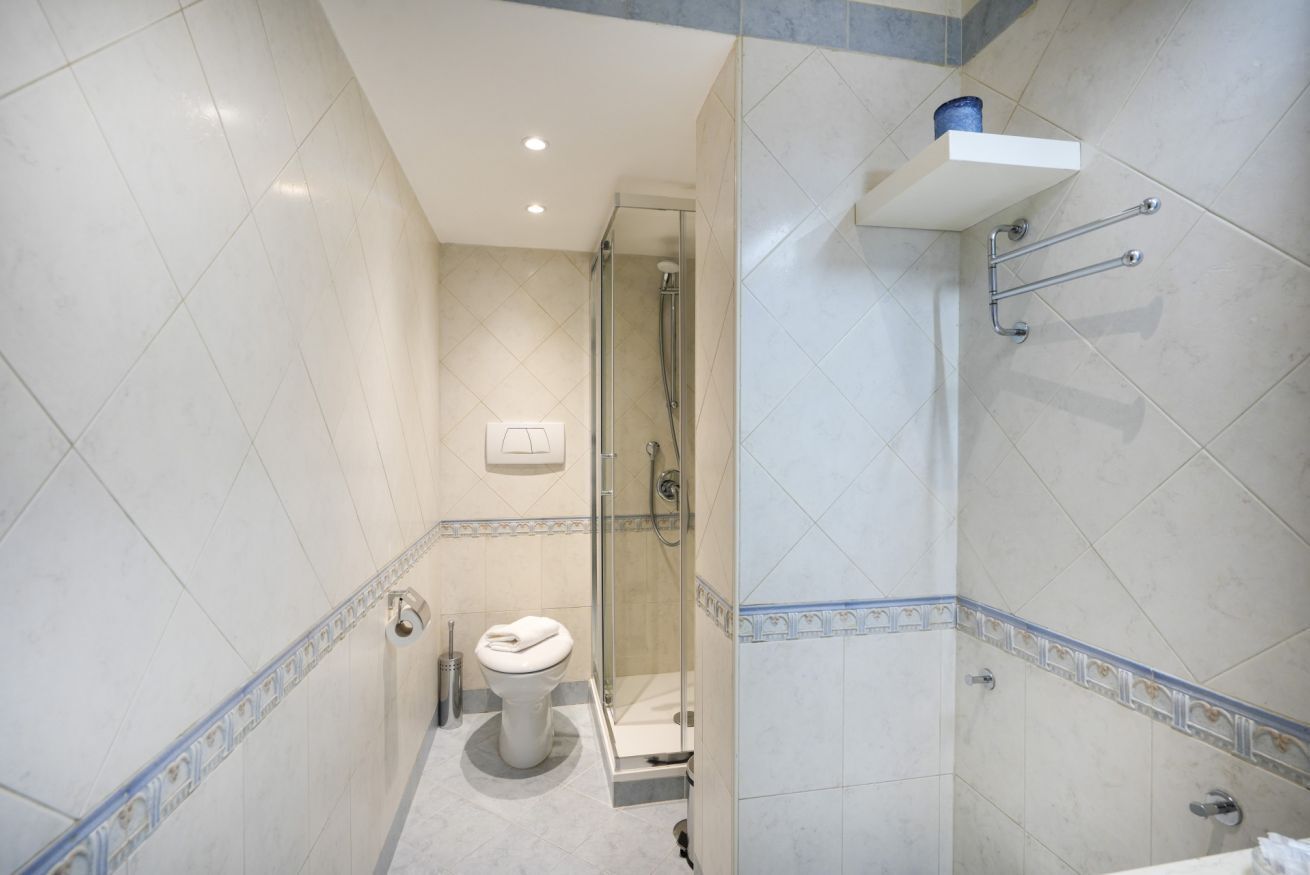 A bathroom with a toilet, shower, and a shelf with a roll of toilet paper.