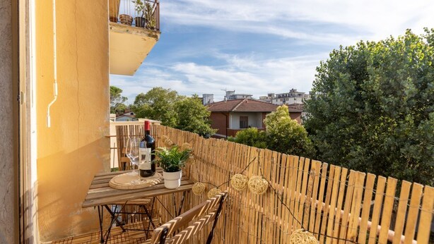 A balcony with a table and chairs, a potted plant, and a bottle of wine. - GuestHost - Porta a Lucca - Pisa Bright Apartment with Balcony (Pisa)