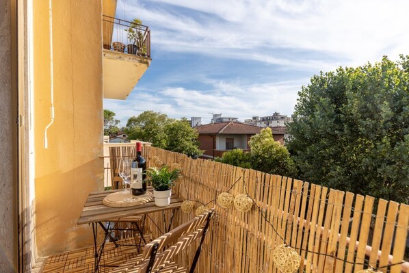 A balcony with a table and chairs, a potted plant, and a bottle of wine.