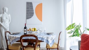 A dining area with a table set for four, a wine bottle, fruit, and a pitcher. A white statue is on the left, and a plant is on the right. - GuestHost - Porta a Lucca - Pisa Bright Apartment with Balcony (Pisa)