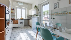 A modern kitchen with a washing machine, a dining table with chairs, and a window with a view. - GuestHost - Porta a Lucca - Pisa Bright Apartment with Balcony (Pisa)