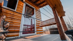 A log cabin with a wooden exterior, a glass door, and a balcony. - Cozy Big Lake Cabin + Private Spa House, Hot Tub & Sauna (Wasilla)