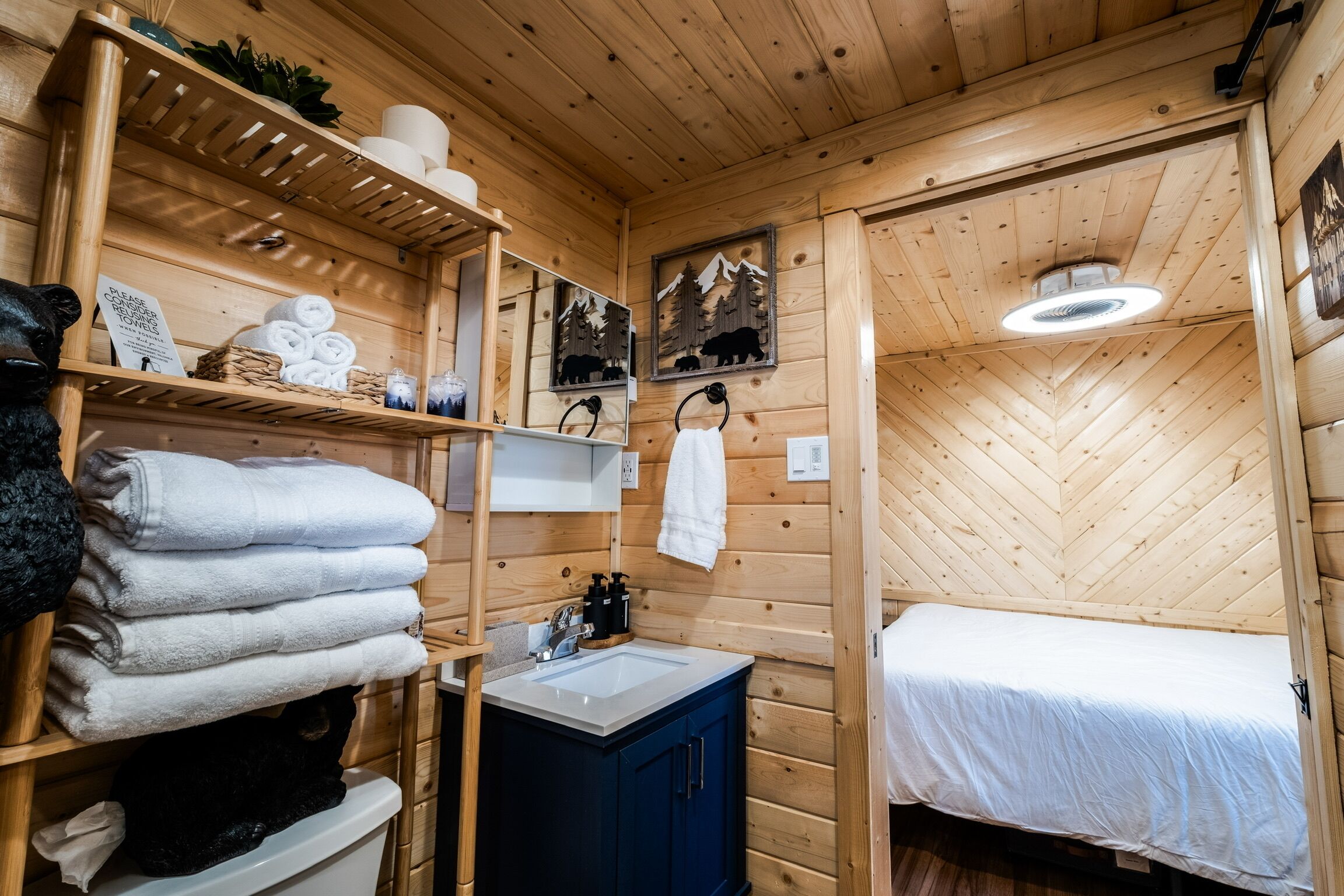 A wooden cabin room with a bed, a sink, and shelves with towels and toiletries.
