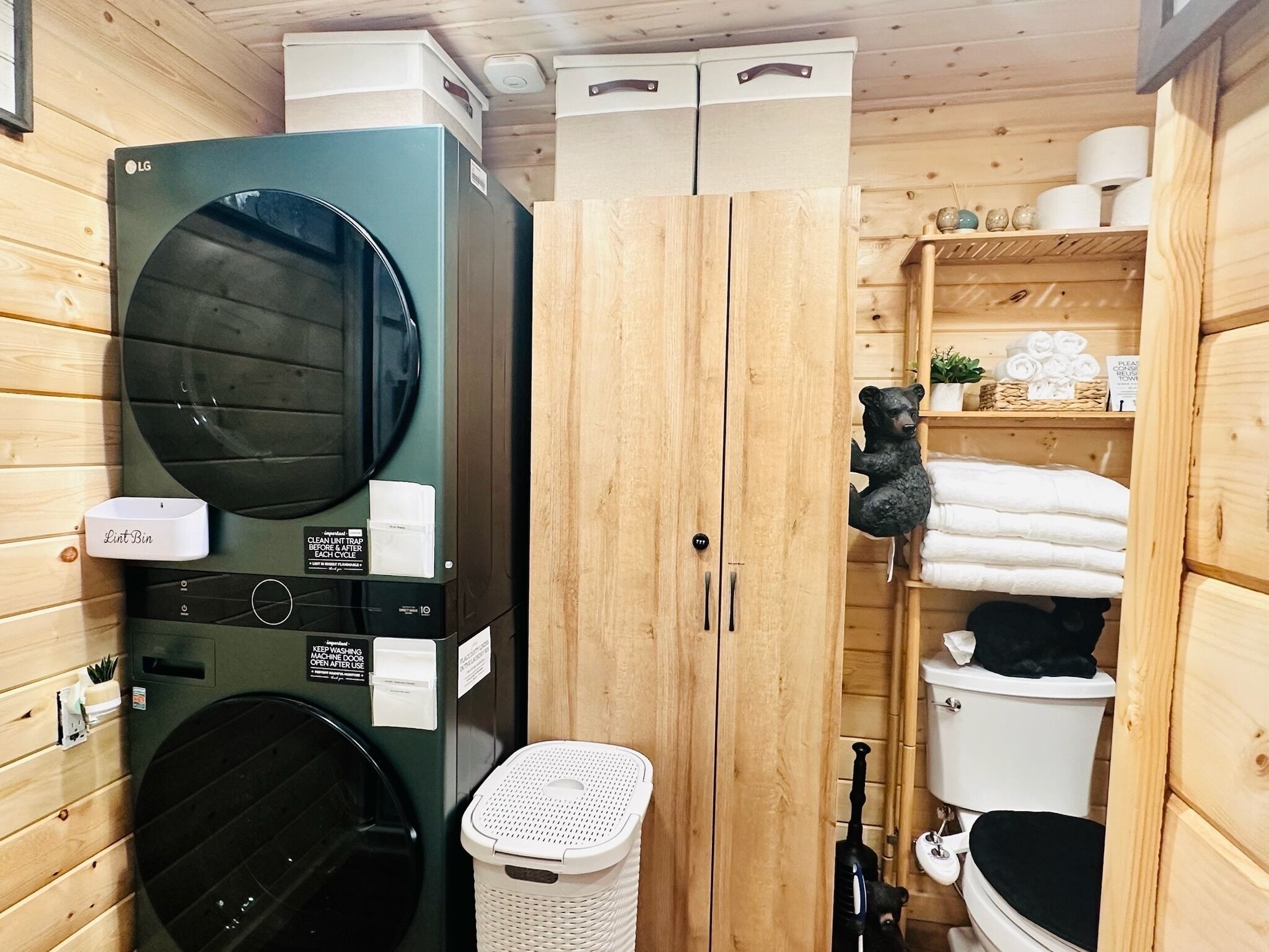 Ett litet och praktiskt tvättrum med en tvättmaskin och en torktumlare med frontmatning, en behållare för ludd, en korg och ett träskåp med en björnfigur.