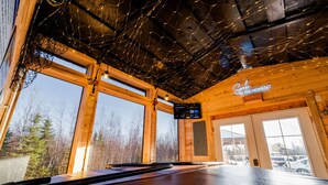 A wooden cabin interior with large windows, a wooden ceiling, and a neon sign that reads "Go with the flow." - Cozy Big Lake Cabin + Private Spa House, Hot Tub & Sauna (Wasilla)