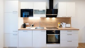 A modern kitchen with white cabinetry, a built-in oven, a microwave, and a coffee machine. - Modernes Apartment mit Terrasse am Klopeiner See (Unterburg am Klopeiner See)