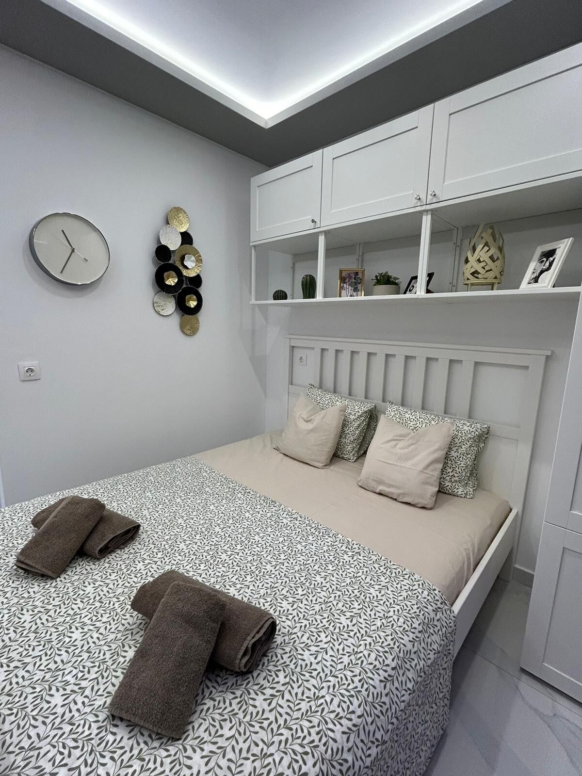 Ein modernes Schlafzimmer mit Bett, weißen Schränken, einer Wanduhr und Dekorationselementen.