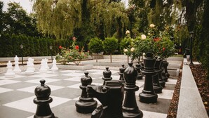 A chessboard with black and white pieces set up outdoors, surrounded by trees and flowers. - Kavaliershaus Erdgeschoss mit Eigener Terrasse im Henriettenhof (Grömitz)