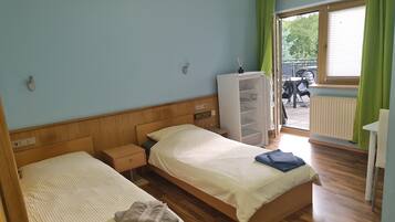 A hotel room with two beds, a wooden headboard, a small bedside table, a white wardrobe, and a view of the outside.