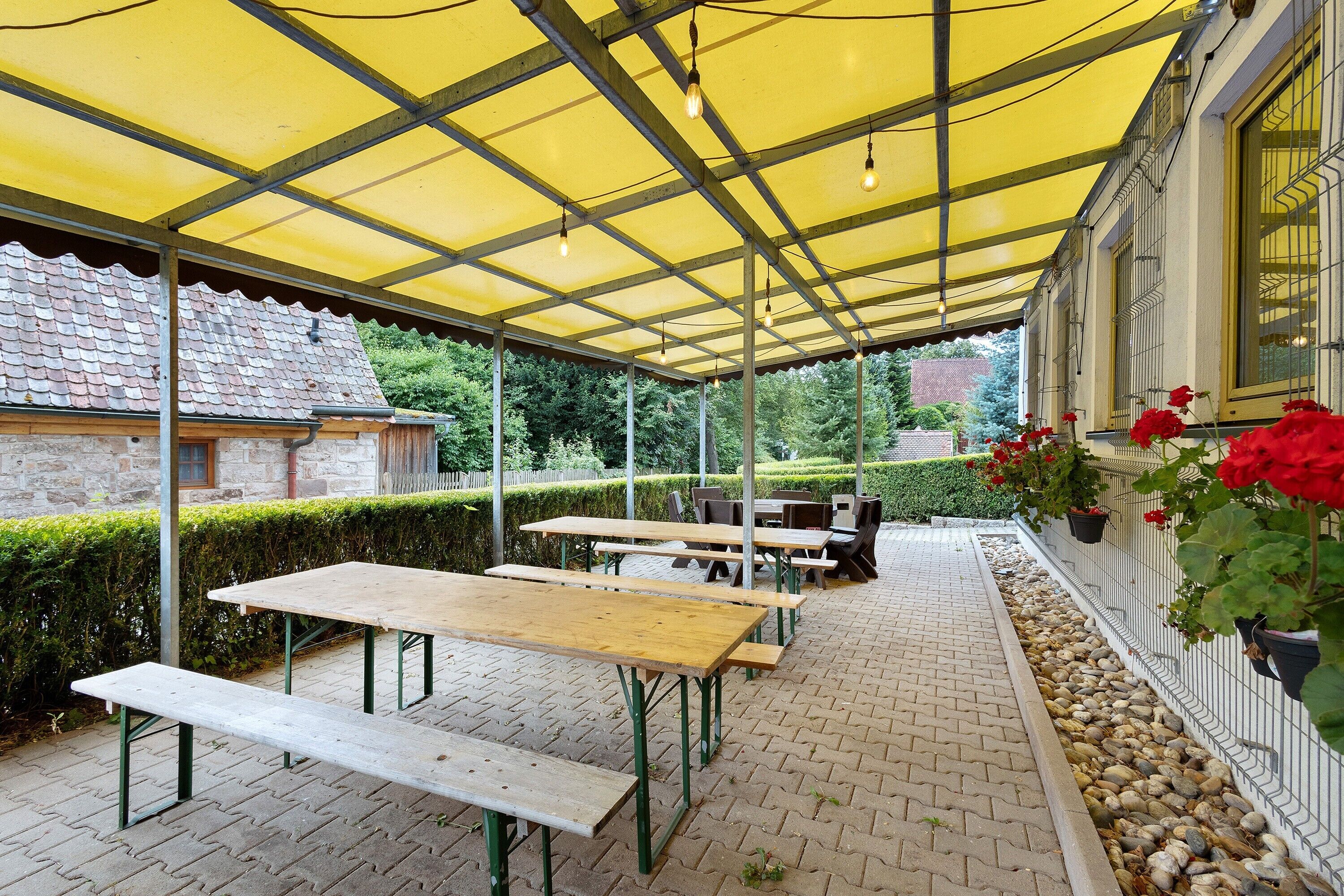 An outdoor patio with tables and benches, a yellow canopy, and a stone building in the background.