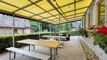 An outdoor patio with tables and benches, a yellow canopy, and a stone building in the background.