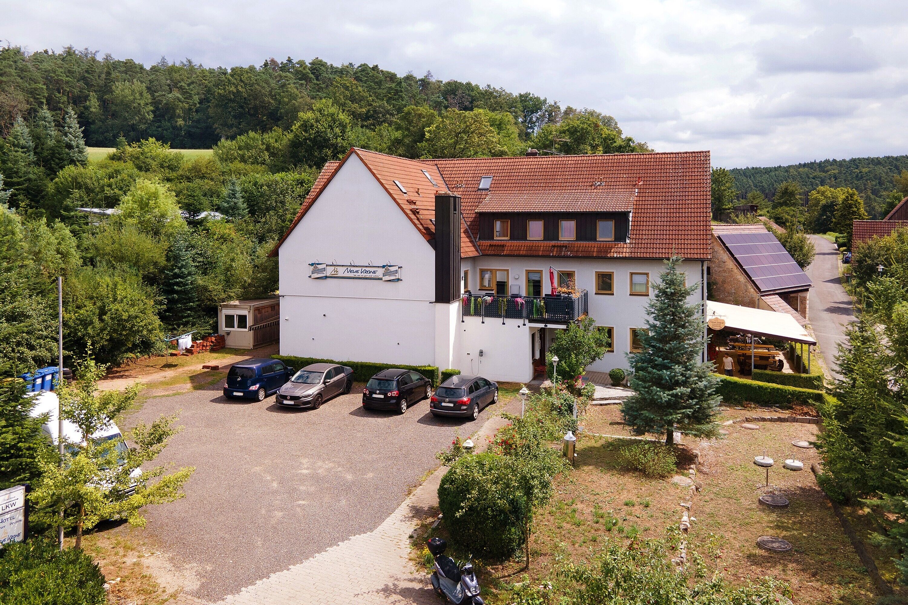 A building with a sloped roof, a sign reading 'La Maison de la Nature,' and a parking area with several cars.