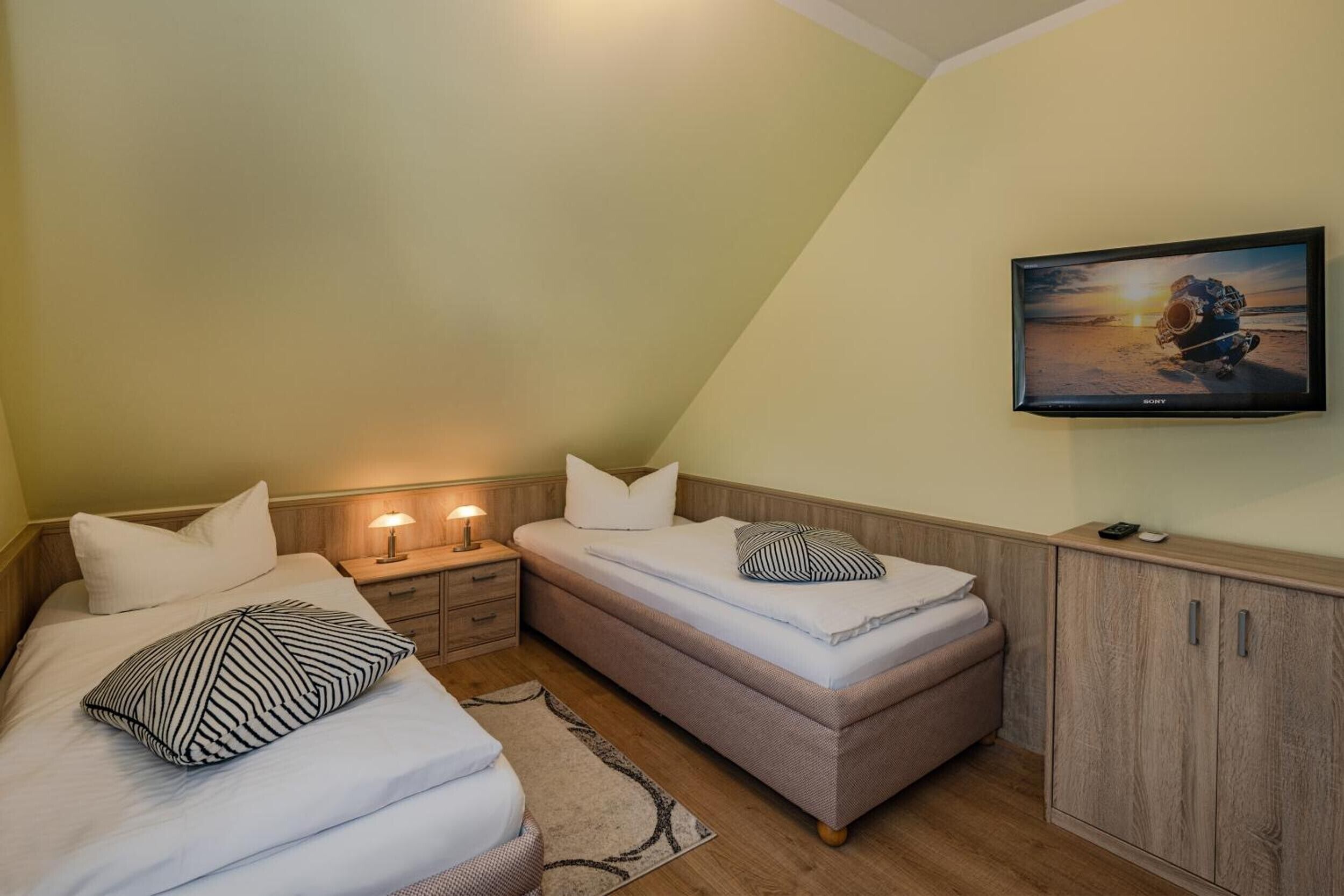 Een slaapkamer met twee bedden, een televisie, een nachtkastje en een kast.