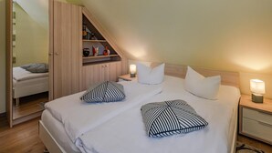 Ein Schlafzimmer mit einem Bett, zwei Nachttischen, einem Schrank und einer schrägen Decke.