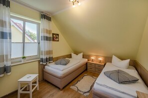 A bedroom with two beds, a small table, a bedside lamp, and a window with curtains.