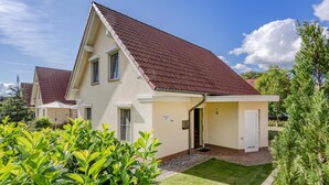 Ein zweigeschossiges Haus mit rotem Ziegeldach, einer Haustür und einer kleinen Veranda.