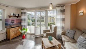Ein Wohnzimmer mit einer Couch, einem Couchtisch, einem Fernseher, einem Holzkabinett und einem Fenster mit Vorhängen.