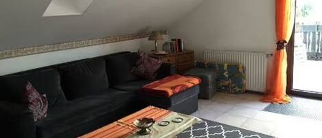 Un salon avec un canapé, une table basse, un radiateur et une fenêtre avec des rideaux.