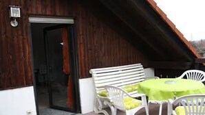 A wooden building with a door, white outdoor furniture, and a green tablecloth.