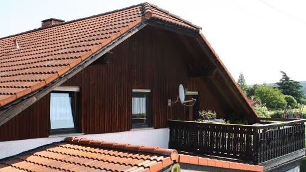 A wooden building with a sloped roof, a balcony with a railing, and a satellite dish.