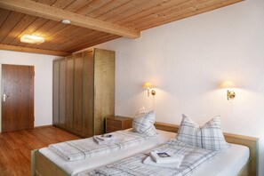 A double bed with patterned bedding, two wall-mounted lamps, a wooden wardrobe, and a small bedside table.