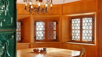 A wooden-paneled room with a chandelier, a table with a pumpkin decoration, and a window with a geometric pattern.