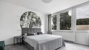 Un dormitorio con una cama, una obra de arte circular en la pared, una ventana y un radiador.