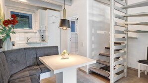 Una cocina moderna con gabinetes blancos, una zona de comedor con una mesa blanca y un sofá gris, y un rascador para gatos.