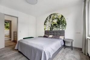 A modern bedroom with a large bed, a round wall art piece, and a view of a wooden staircase.
