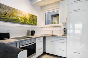 A modern kitchen with white cabinetry, a built-in oven, a coffee maker, and a painting of a forest scene.
