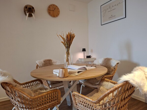 Una mesa redonda de madera con sillas, un jarrón con plantas secas, un libro y una taza.