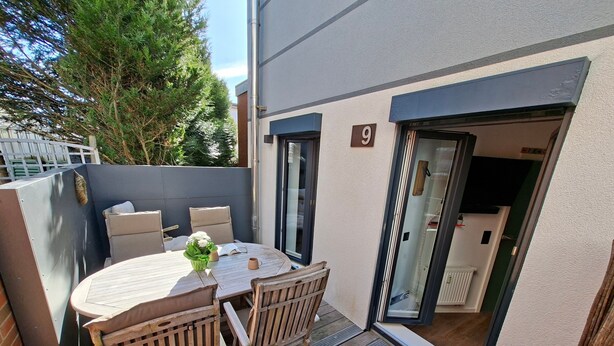 Eine Terrasse mit einem runden Tisch, vier Stühlen und einem kleinen Topfpflanzen.