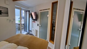 Ein Schlafzimmer mit einem Bett, einem an der Wand montierten Fernseher und einer Schiebeglastür, die zu einem Außenbereich führt.