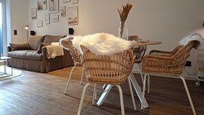 Ein Wohnzimmer mit einer Couch, zwei Korbstühlen, einem Couchtisch und einer Wanduhr.