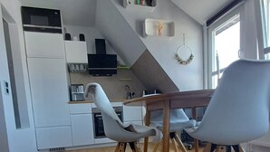 Eine moderne Küche mit weißen Schränken, einer Mikrowelle und einem Einbauofen. Es gibt einen Essbereich mit einem Holztisch und zwei Stühlen.