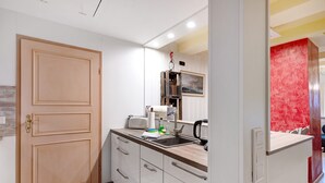 A compact kitchen with a wooden door, white cabinets, a countertop, a sink, and a red accent wall.