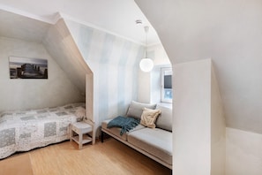Ein Schlafzimmer mit schräg verlaufender Decke, einem Bett, einer Couch, einem kleinen Tisch und einer Pendelleuchte.