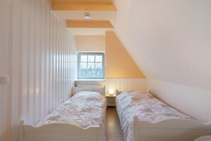 Une petite pièce avec deux lits simples, une fenêtre et une lampe.