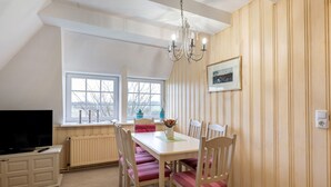Un espace repas comprenant une table, des chaises, un lustre, un téléviseur et une fenêtre donnant sur un beau paysage.