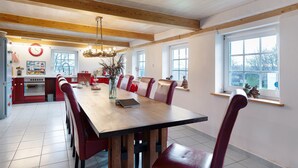 Un comedor con mesa de madera y sillas rojas, una cocina al fondo y una ventana con vistas.