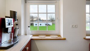 Una cocina con cafetera, ventana con vistas a una casa y encimera de madera.